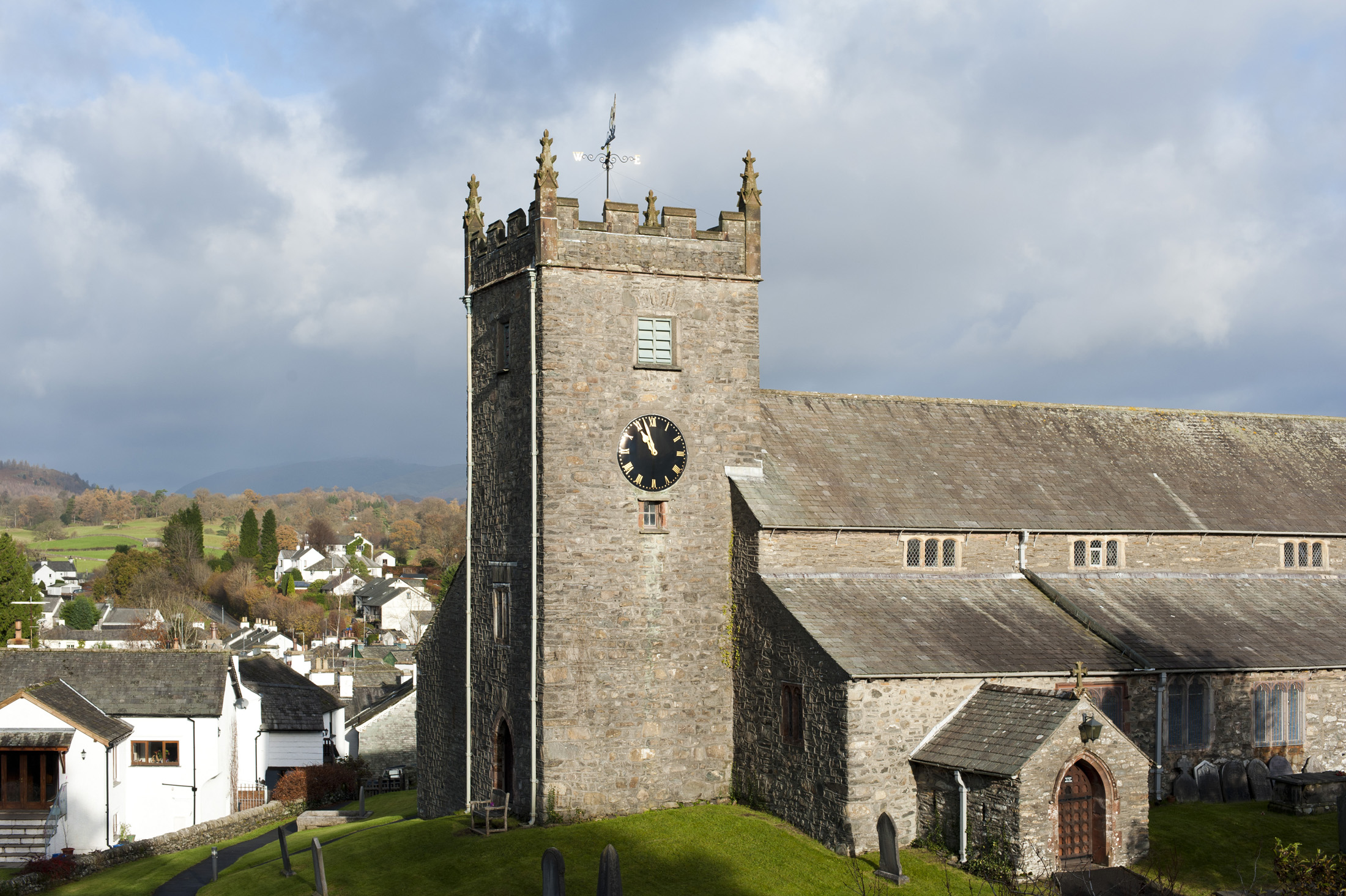 an image of View of the old stone building and clock tower of St Michael and All Angels Church in the quaint whitewashed village of Hawkshead in the Lake District in Cumbria